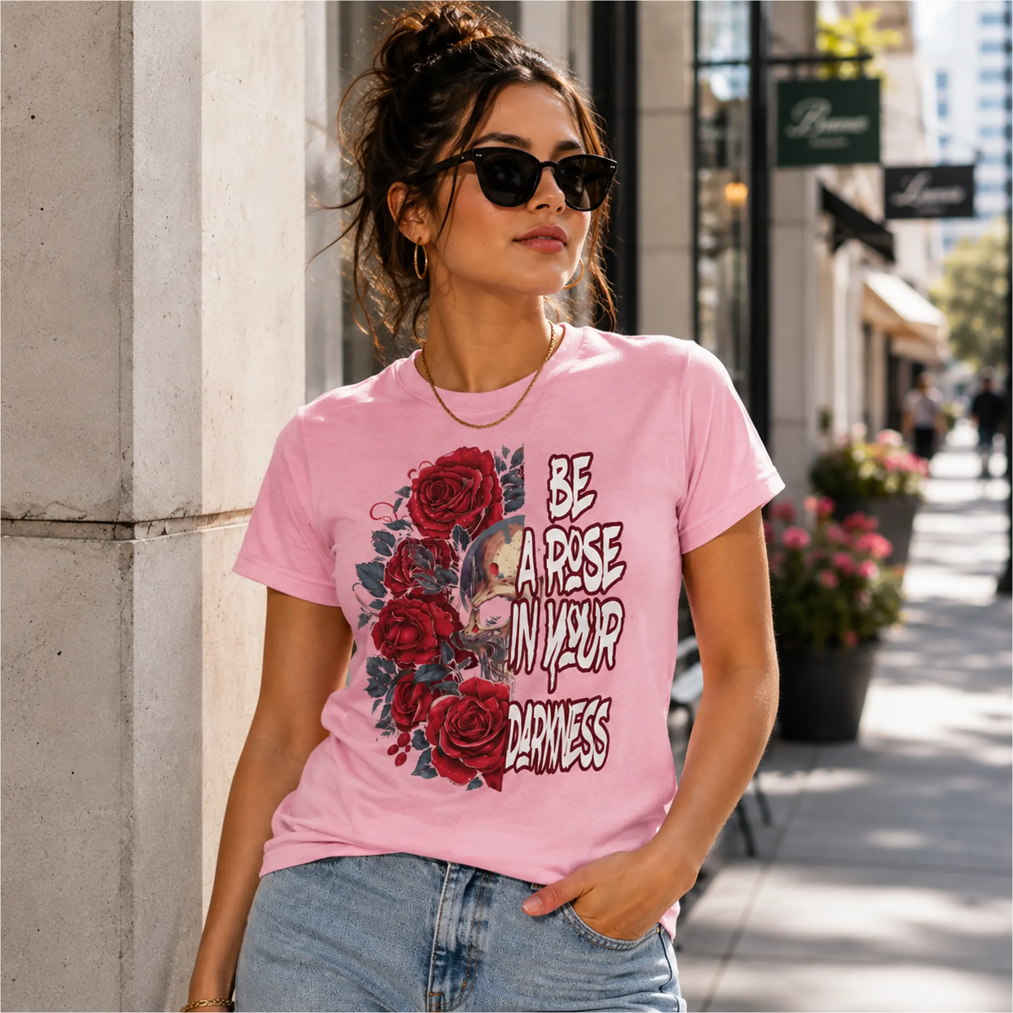 Woman wearing Be A Rose In Your Darkness pink graphic tee with skull and red roses design in an urban shopping district – Black Heart Tees motivational apparel
