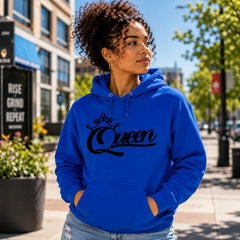 Woman wearing Queen Royal Blue pullover hoodie with black crown script design in a bright urban setting – Black Heart Tees motivational apparel.