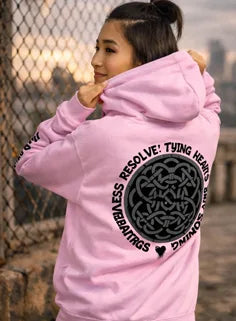 Person wearing a pink hoodie with text design, standing against a chain-link fence.