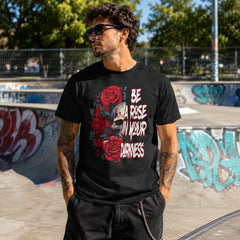 Man wearing Be A Rose In Your Darkness black graphic tee with skull and roses design at a skatepark – Black Heart Tees motivational apparel