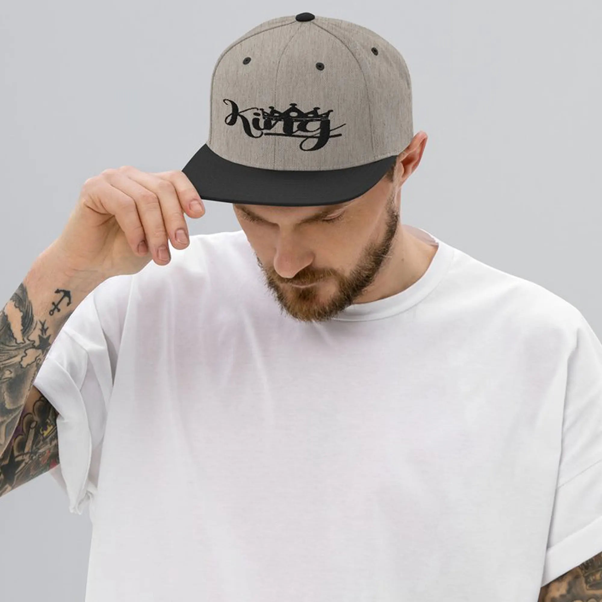 Man wearing a gray and black cap with the King design embroidered on a snapback hat