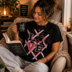 Woman wearing Love Coffee black graphic tee reading with a coffee mug in a cozy reading nook – Black Heart Tees motivational apparel