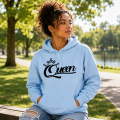 Woman wearing Queen light blue pullover hoodie with black crown script design in a bright outdoor park – Black Heart Tees motivational clothing.
