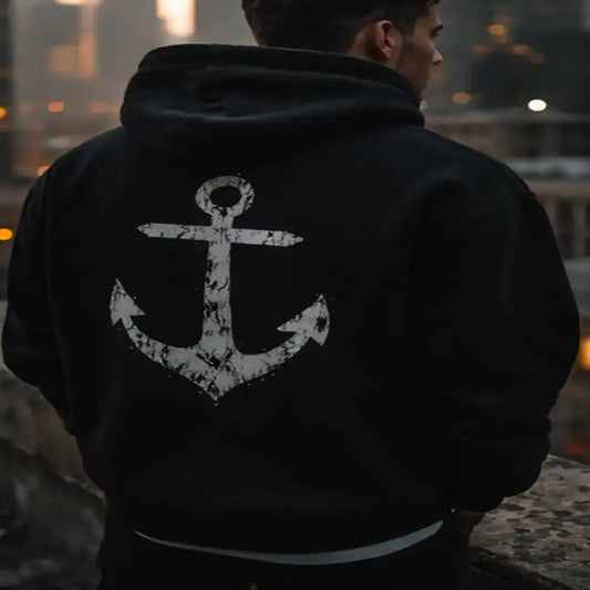 Person wearing a black hoodie with an anchor design, standing against a blurred background.